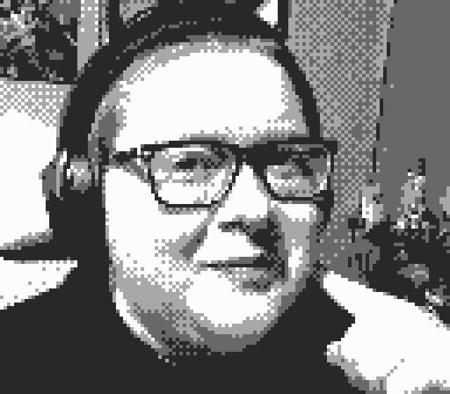 A Gameboy Camera-style picture of the Webmaster from the shoulders up. They are smiling at the camera.